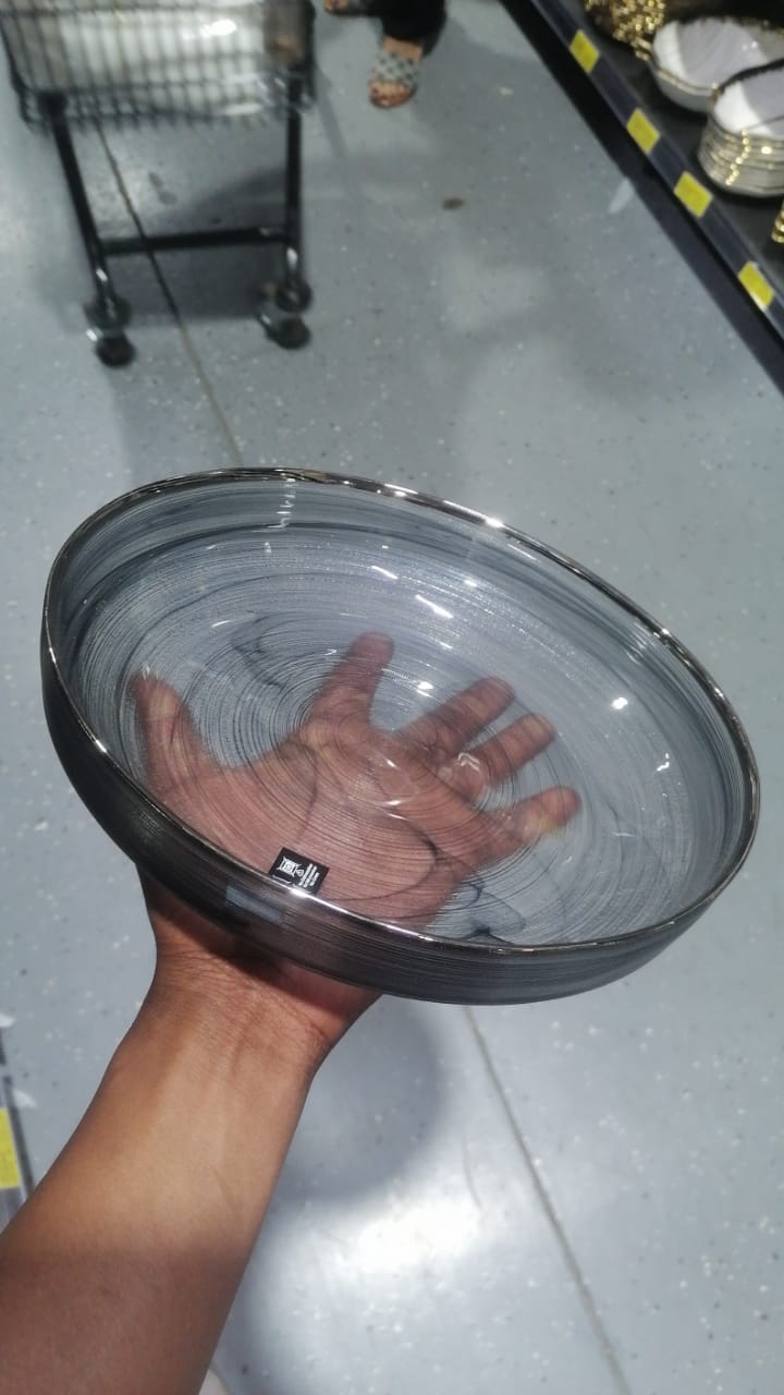 Black glass dinner plate with subtle gray swirl design and silver rim, stacked on display.
