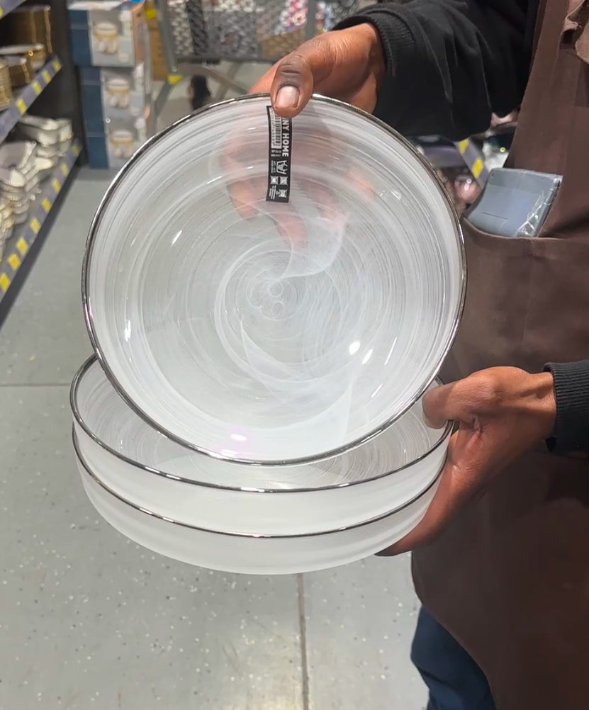 Clear glass dinner plate with subtle white swirl design and silver rim, stacked on display.